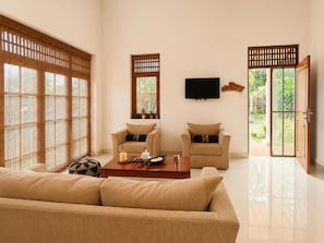 A living room with a sofa, two armchairs, a coffee table, a TV, and sliding doors leading to a garden. - Seahorse Villas - Three-Bedroom Apartment (NEGOMBO)