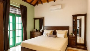 A hotel room with a bed, a wardrobe, a mirror, a bedside table, and a window with curtains. - Seahorse Villas - Three-Bedroom Apartment (NEGOMBO)