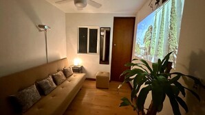 Sala de estar com sofá, ventilador de teto, planta e tela de projeção exibindo uma paisagem.
