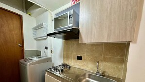 Cozinha compacta com micro-ondas integrado, fogão a gás e pia de aço inoxidável.