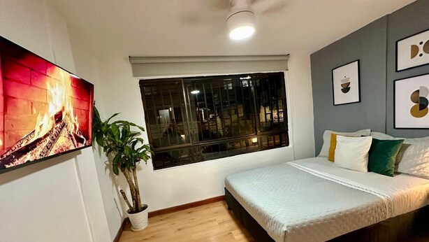 Quarto com cama, janela, ventilador de teto e TV fixada na parede.