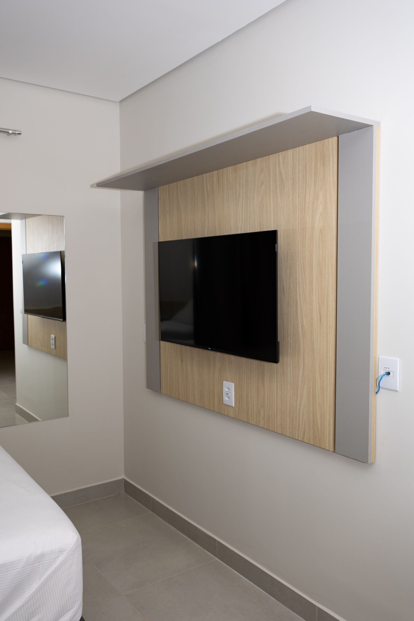 A modern hotel room with a mounted flat-screen TV, a bed, and a mirror.