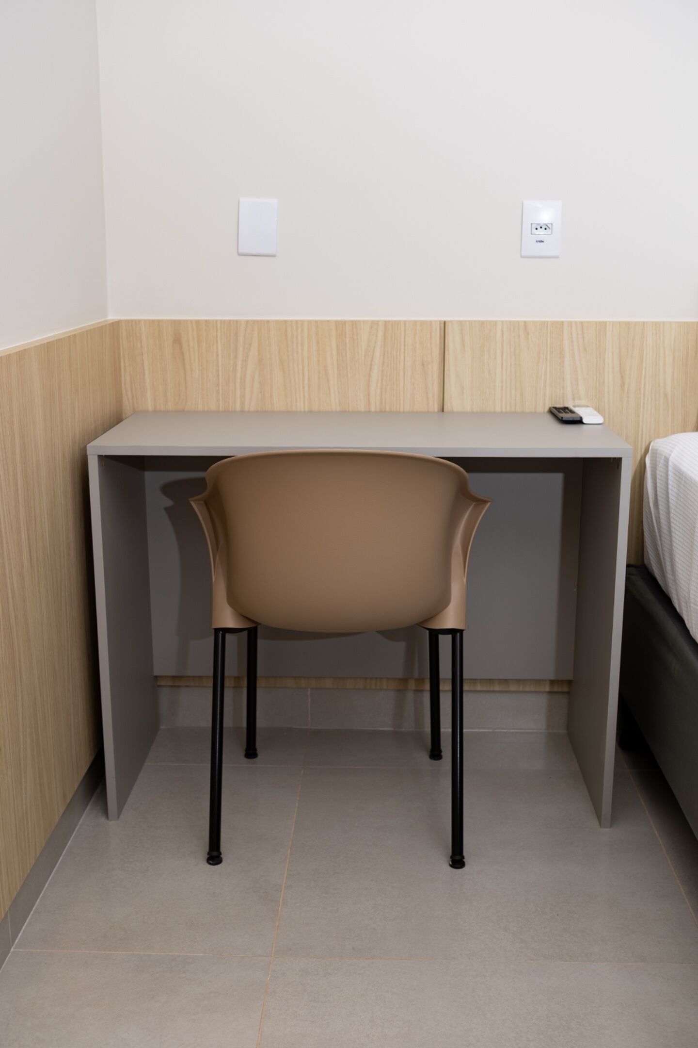 A small, modern room with a desk and chair, a bed, and a wall socket.