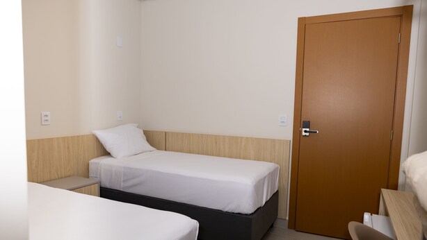 A small, compact room with a single bed, a bedside table, and a door. - Ex Hotels Laguna  (Inocência)