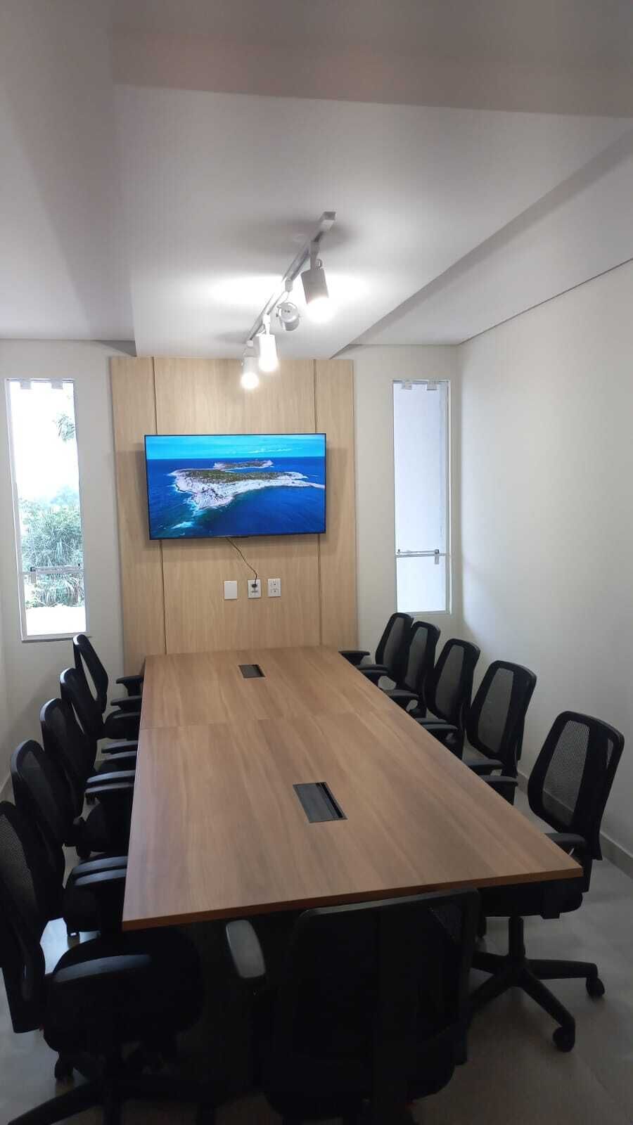 A conference room with a long table, black office chairs, a mounted TV, and a ceiling light fixture.