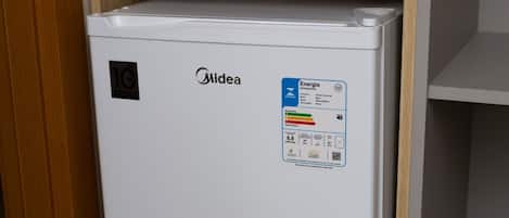 A compact white refrigerator with a Midea logo, a sticker indicating energy efficiency, and a small shelf above it.
