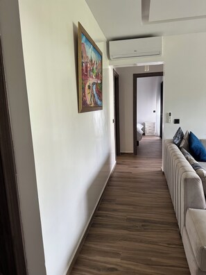 Ein Flur mit Holzboden, einem Gemälde an der Wand, einer Klimaanlage und einem Sofa mit Kissen.