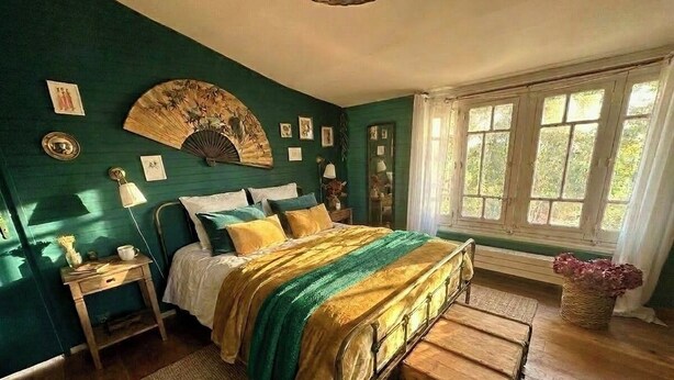 Een slaapkamer met een bed, nachtkastje, lamp en een raam met gordijnen.