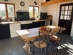 A kitchen with a wooden table, chairs, and a fruit bowl. - Guest house immersed in nature with horses and donkeys (Jouques)