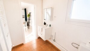 A bathroom with white fixtures, a window, and a view into another room.