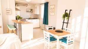A modern kitchen with a central island, a dining area with a wooden table and white chairs, and a view of the adjacent living space.