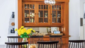 Zona pranzo con tavolo in legno, sedie nere e un mobile con ante in vetro contenente stoviglie.