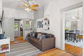 Ein geräumiger Wohnbereich mit einem braunen Sofa, einem Deckenventilator und einem Essbereich mit einer Chandelier.