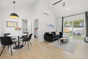 Ein modernes Wohnzimmer mit einer schwarzen Couch, einem Couchtisch und einem Essbereich mit rundem Tisch und Stühlen.