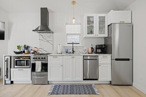 Eine kompakte Küche mit weißen Schränken, einem Edelstahlherd, einer Spülmaschine und einem eingebauten Backofen.