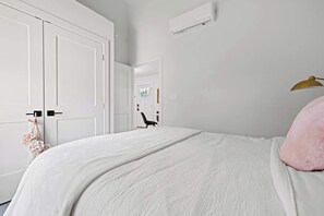 Ein Schlafzimmer mit einem Bett, weißen Wänden, einer Tür und einer Klimaanlage.