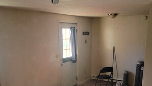 A room with hardwood flooring, a door with a window, a chair, and a small trash can.
