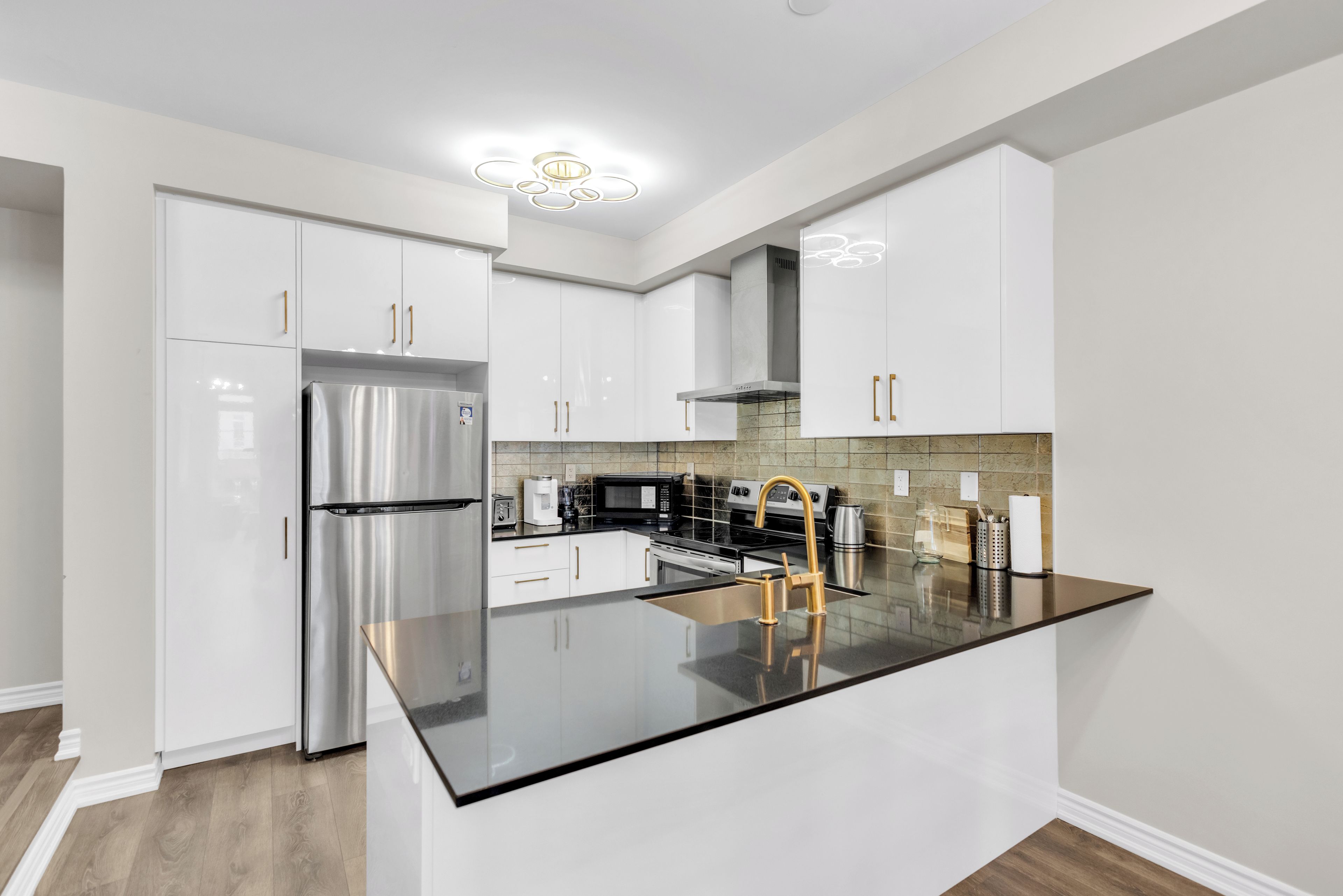 A modern kitchen with white cabinetry, stainless steel appliances, and a black countertop.