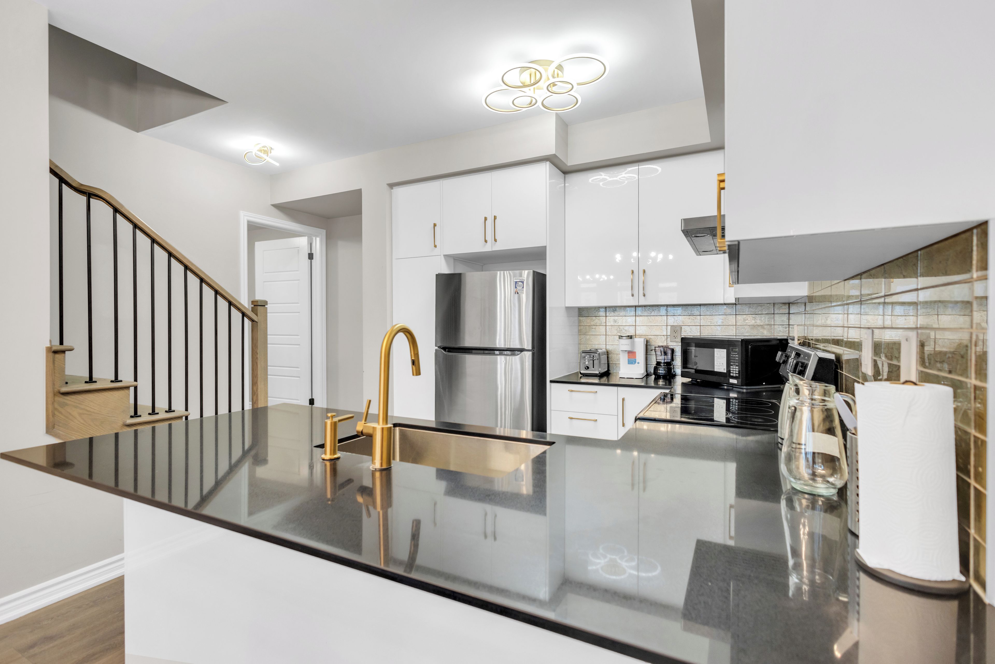 Una cocina moderna con una isla central, electrodomésticos de acero inoxidable y una escalera con detalles de madera.