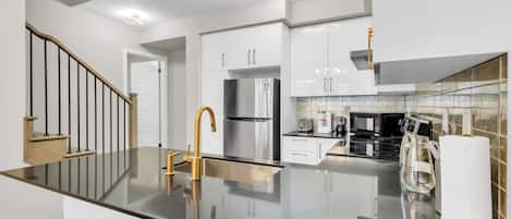 Una cocina moderna con una isla central, electrodomésticos de acero inoxidable y una escalera con detalles de madera.