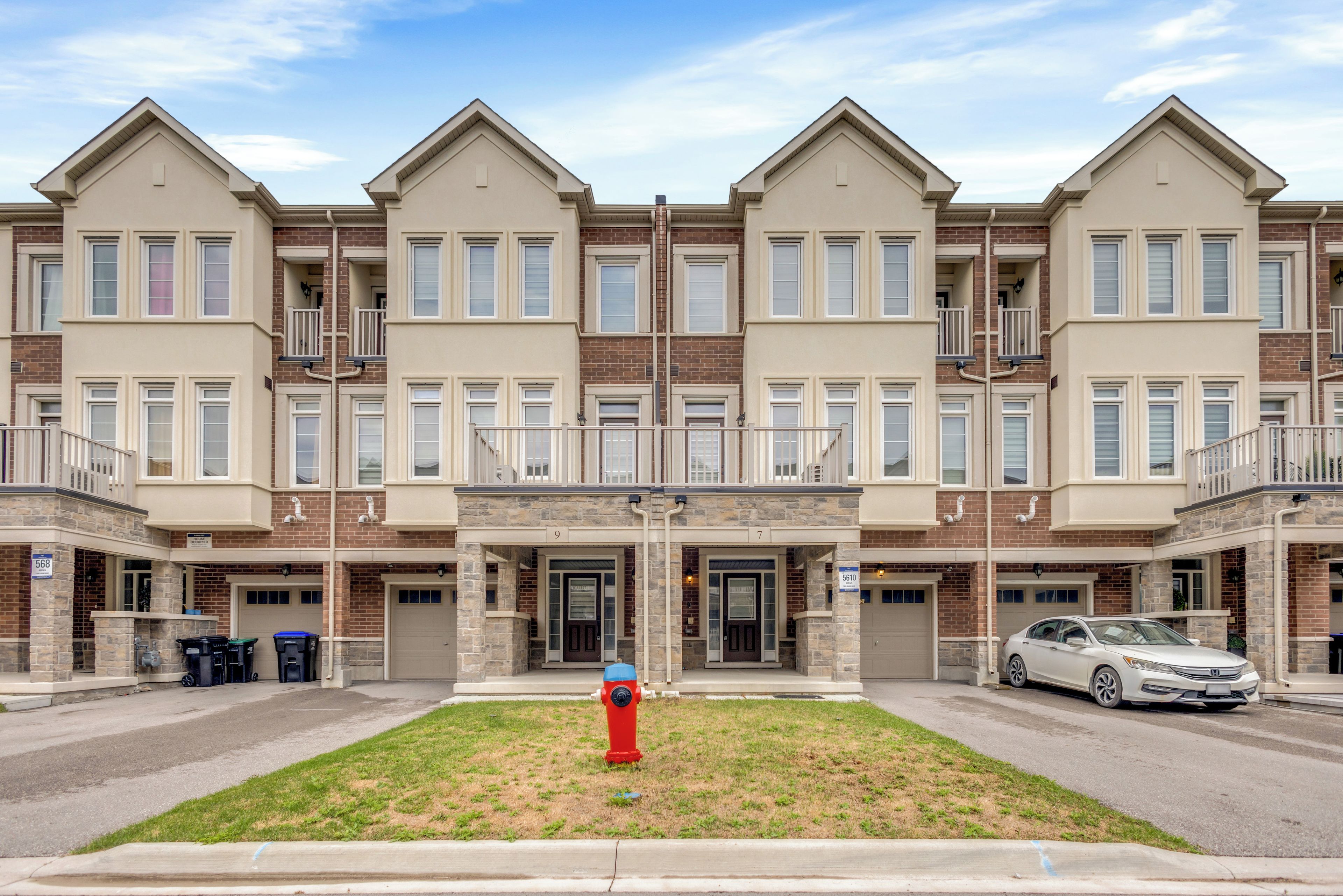 A multi-story residential building with a central entrance, numbered doors, and a fire hydrant in the front yard.