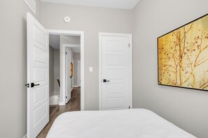 A bedroom with a bed, two white doors, a hallway, and a large abstract painting on the wall.