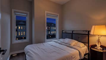 A bedroom with a bed, two windows, a nightstand, and a lamp.