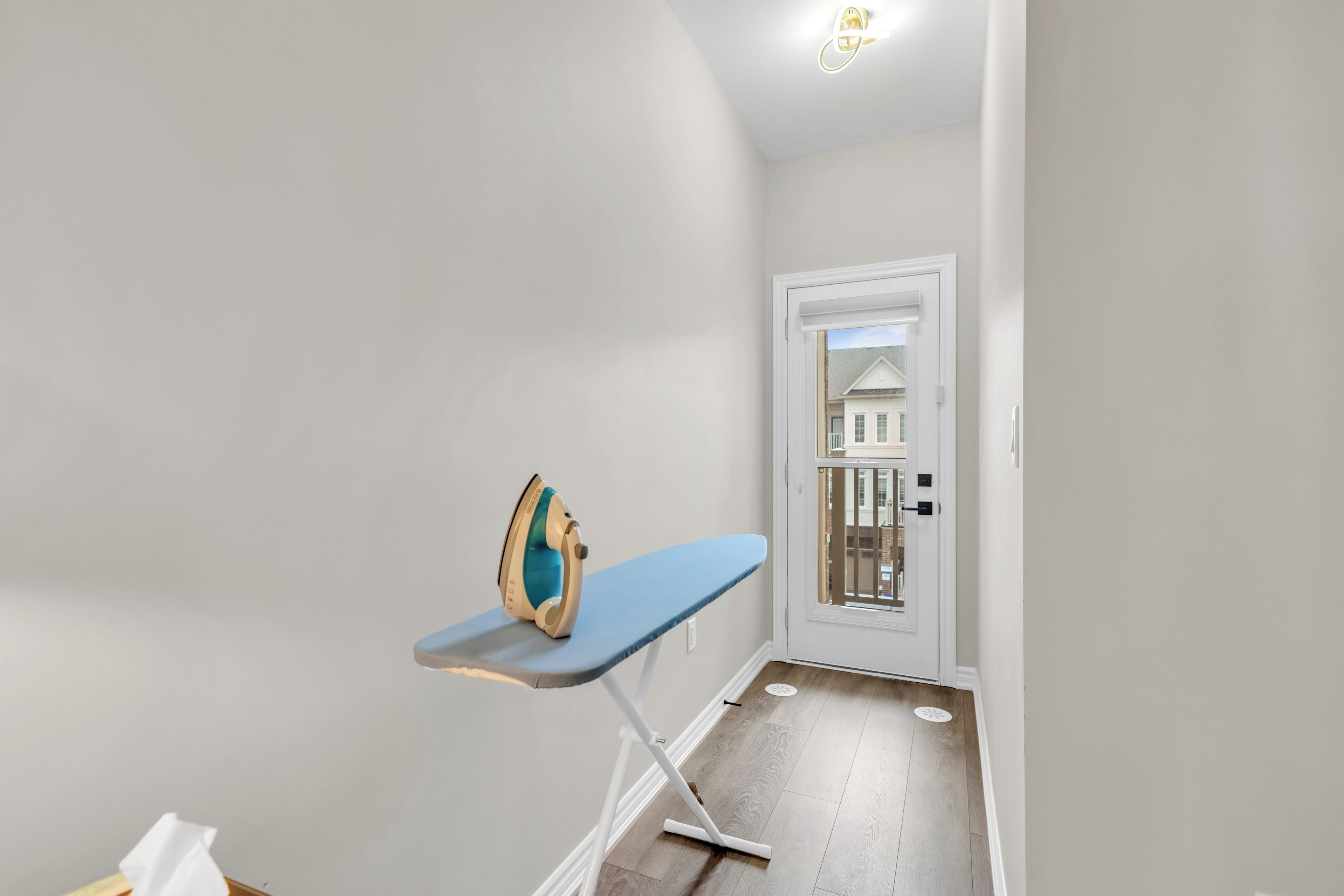A hallway with a white door, a blue ironing board, and a wooden floor.