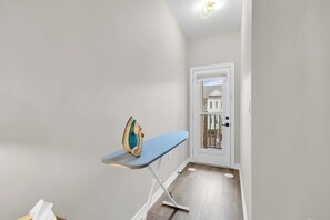 A hallway with a white door, a blue ironing board, and a wooden floor. - Bright 3BR Home with Balcony & Free Parking (Bradford West Gwillimbury)