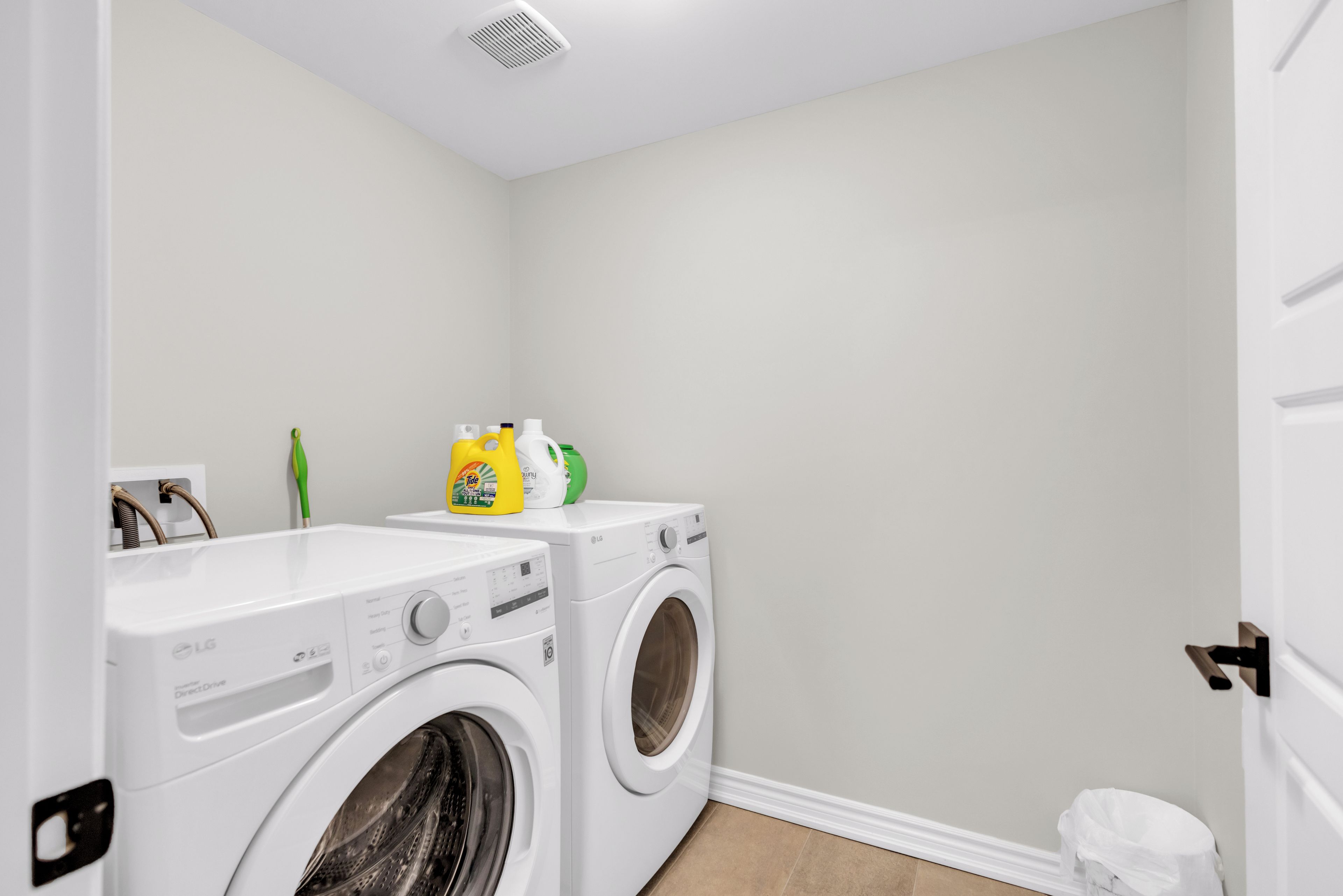 A laundry room with two front-loading washing machines, a white wall, and a door.