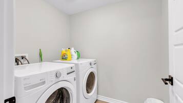 A laundry room with two front-loading washing machines, a white wall, and a door.