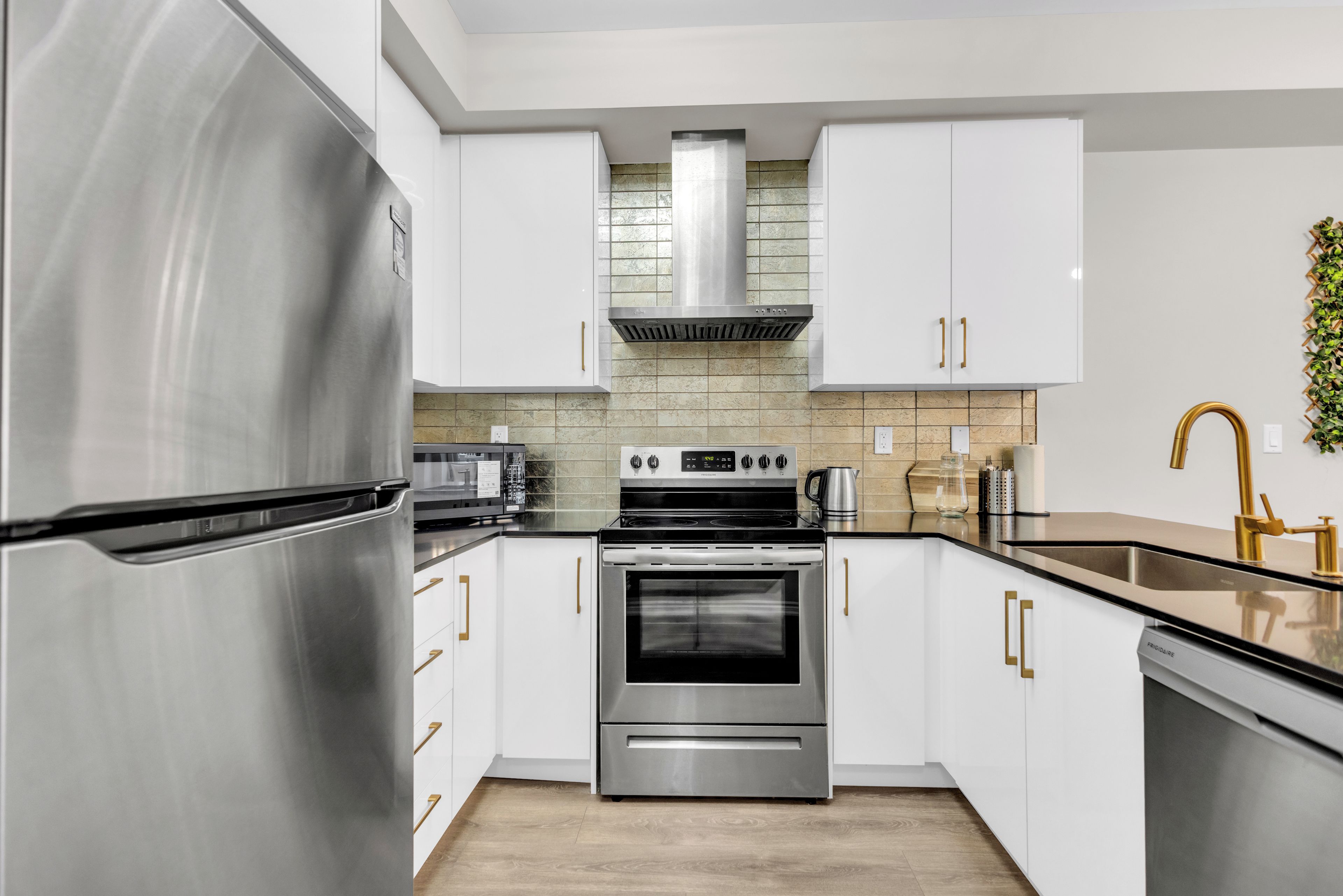 A modern kitchen with stainless steel appliances, white cabinetry, and a wooden floor.