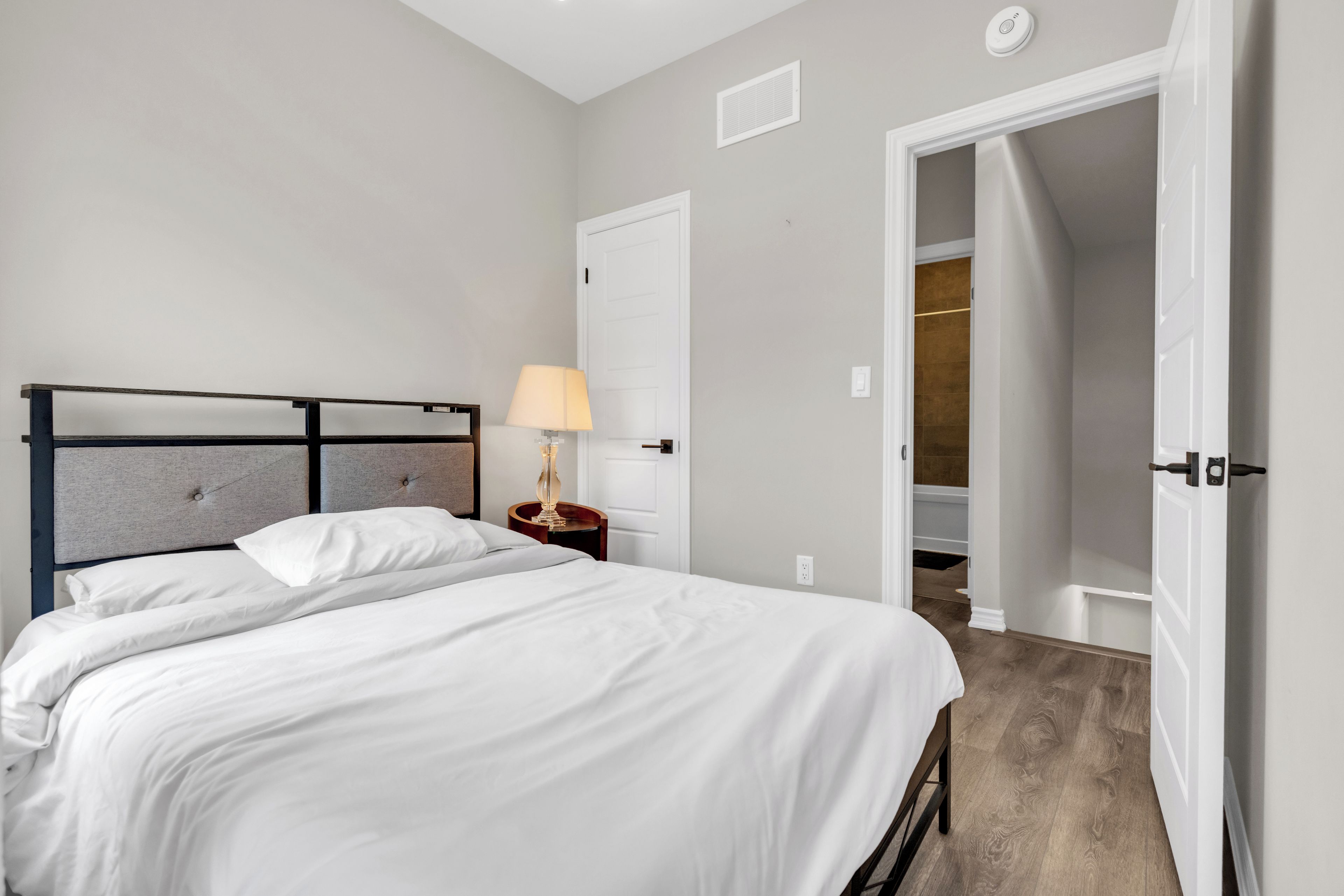 Une chambre d’hôtel avec un lit, une table de chevet, une lampe, une porte et une vue sur la salle de bain.