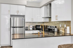 A modern kitchen with stainless steel appliances, white cabinetry, and a central island with a gold faucet.