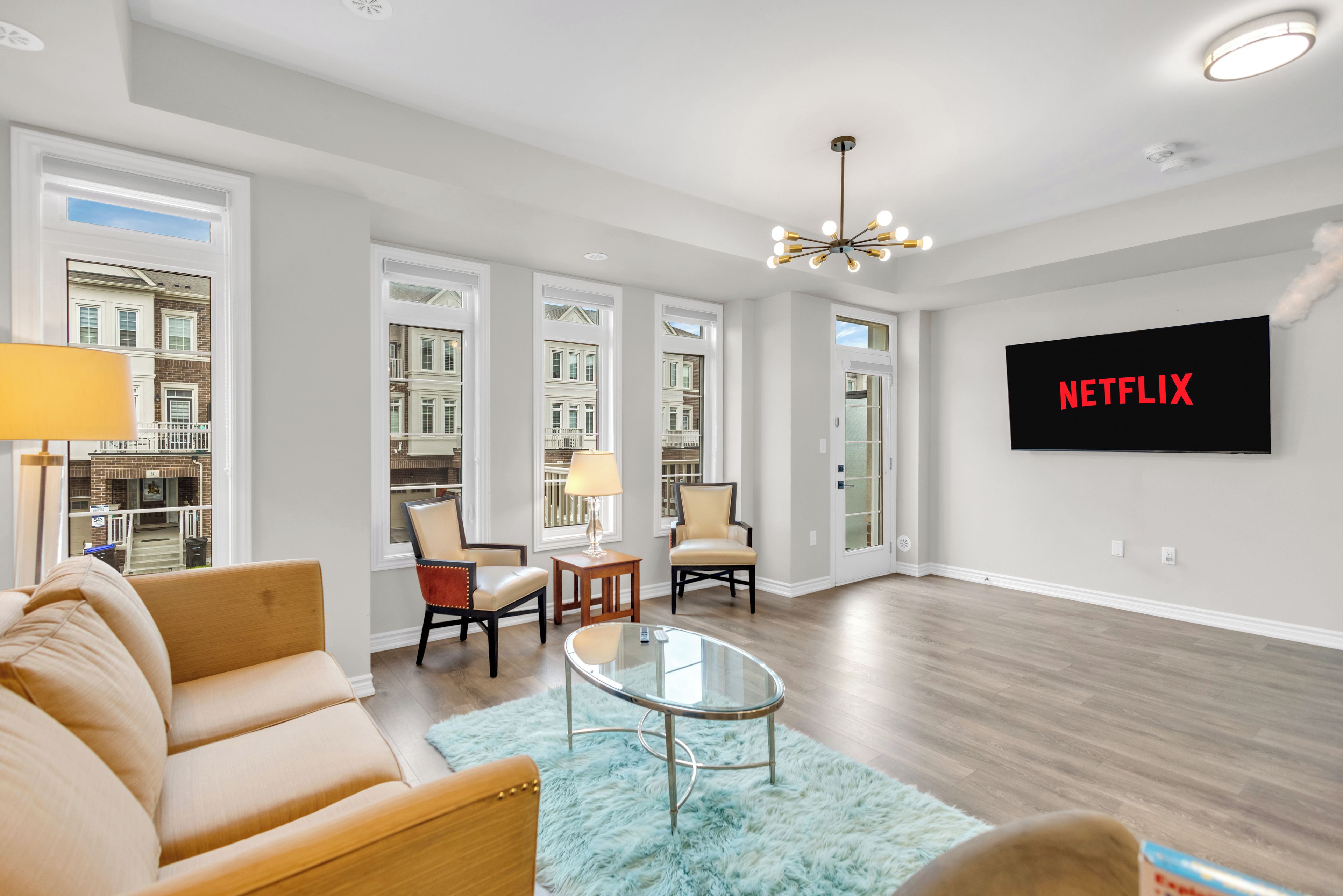 A modern living room with a sofa, chairs, a coffee table, and a TV screen displaying 'NETFLIX'.