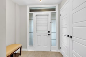 A hallway with a bench, a white door with frosted glass panels, and a light fixture on the ceiling.