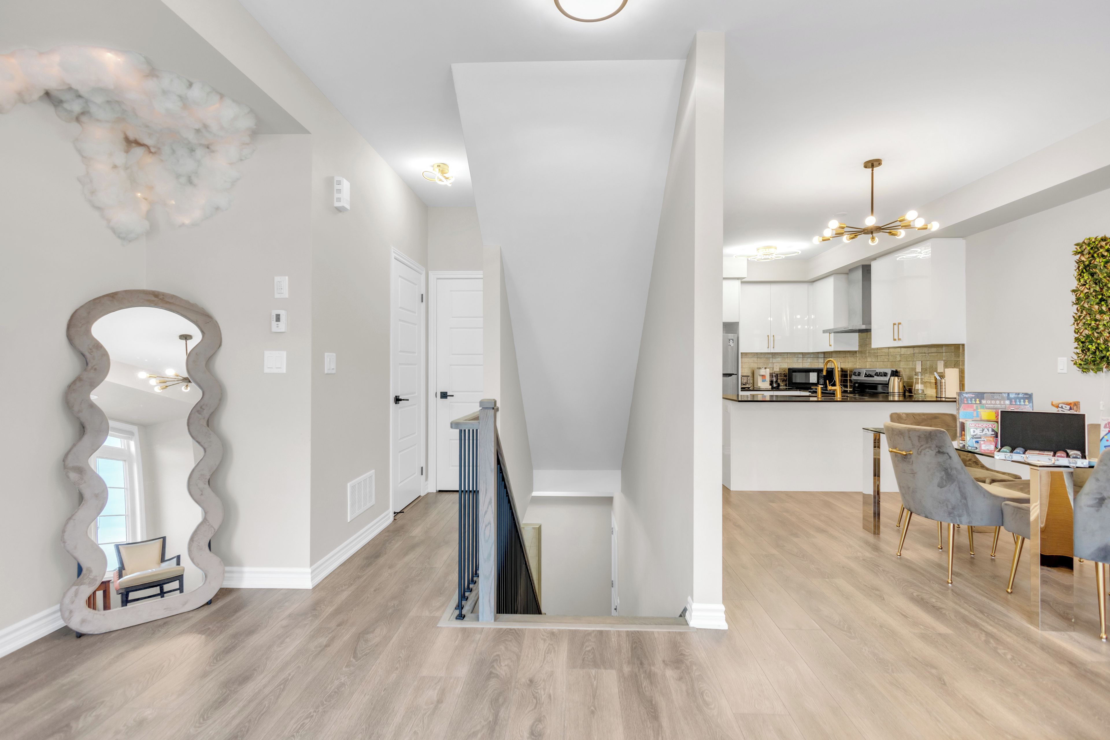 A modern interior with a staircase leading to a dining area, a kitchen with contemporary appliances, and a decorative wall piece.