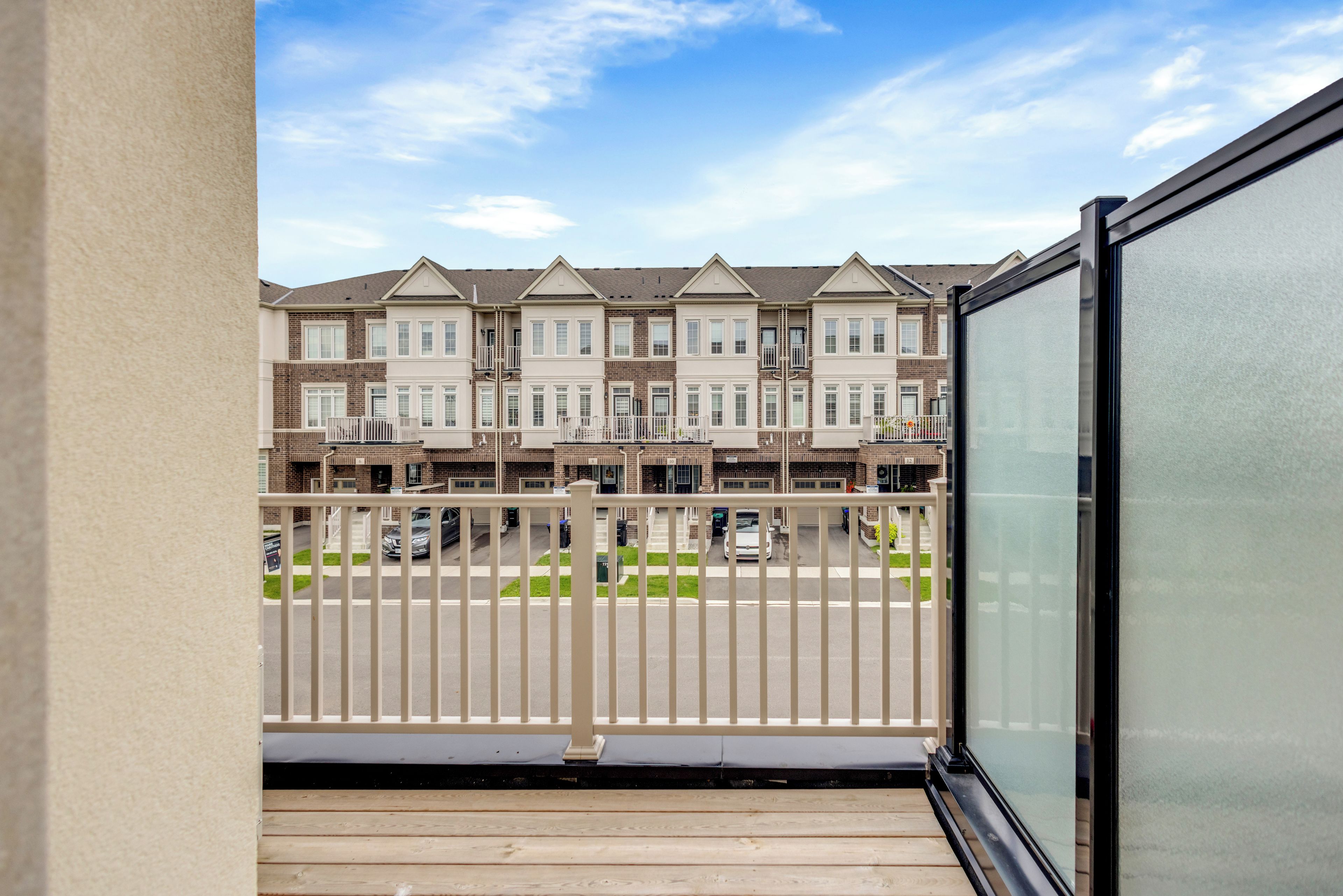 Ein Balkon mit Blick auf eine Reihe von Reihenhäusern, einen eingezäunten Parkbereich und einen wolkenlosen Himmel.