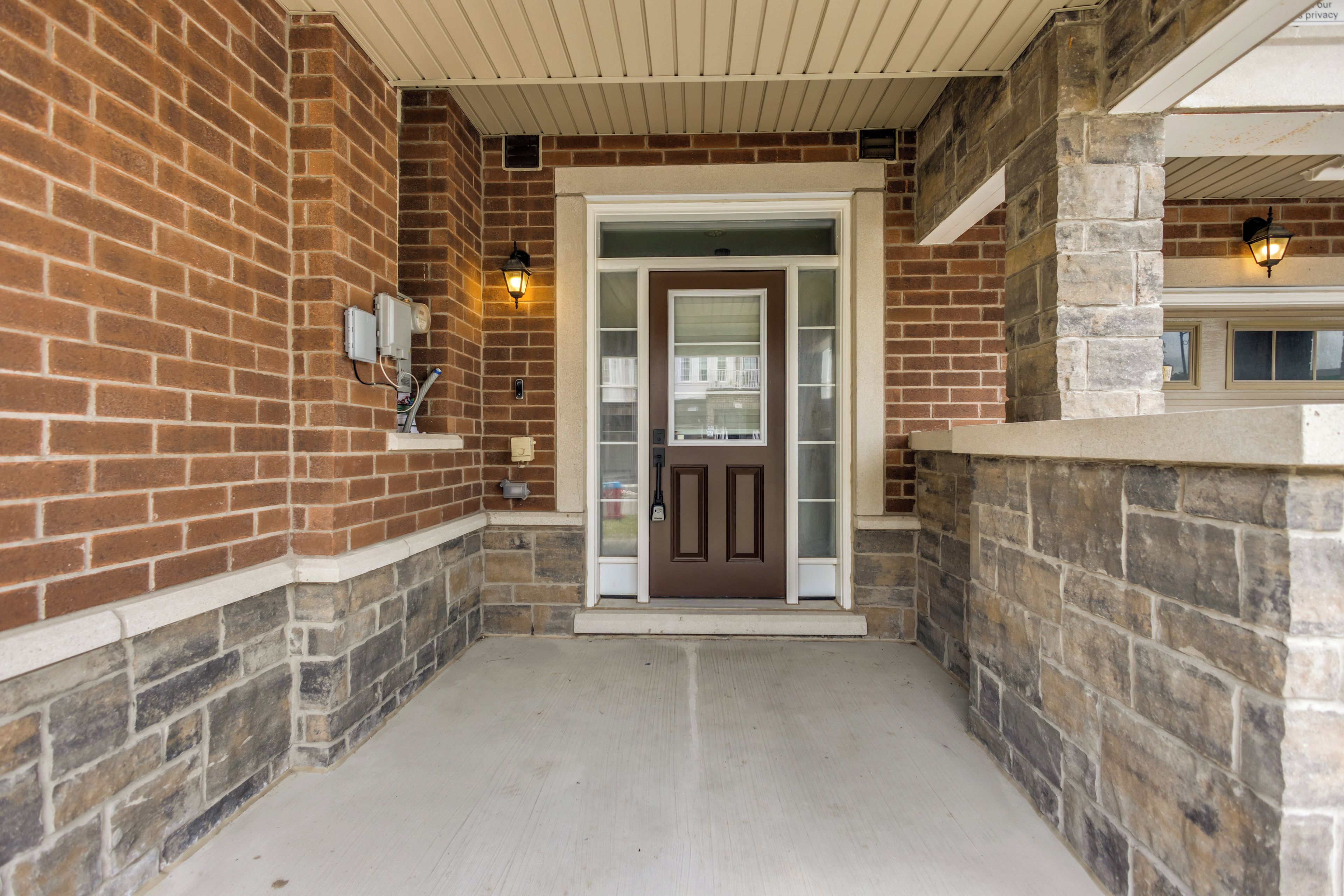 A brick exterior with a stone wall, a door with a glass panel, and a light fixture above it.