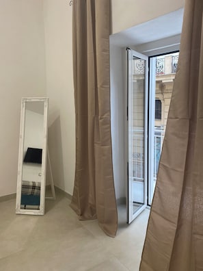 Ein Zimmer mit einem großen Spiegel, beigen Vorhängen und einer Schiebetür zu einem Außenbereich.