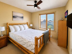 Ein Schlafzimmer mit einem Bett, Deckenventilator, einem Fenster mit Jalousien, einem Fernseher und einem Bild an der Wand.