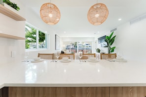 A modern kitchen with a large island, wicker pendant lights, and a view of the street. - Casa del Rio - 2BR on the Intracoastal (Boca Raton)