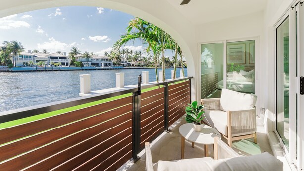 Un balcon donnant sur une étendue d’eau, avec des lattes en bois et une chaise blanche.
