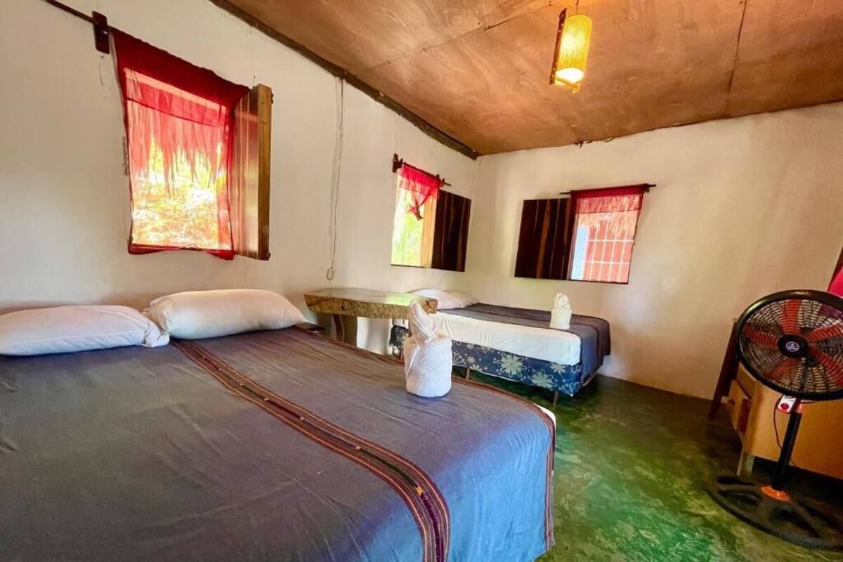 A room with two beds, a table, and a fan.