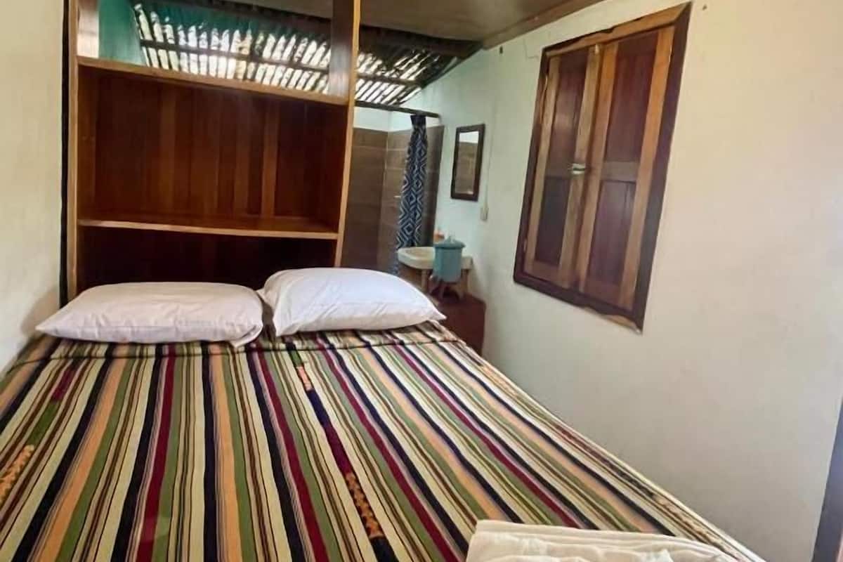 A room with a bed, a wooden headboard, a small table, and a window.