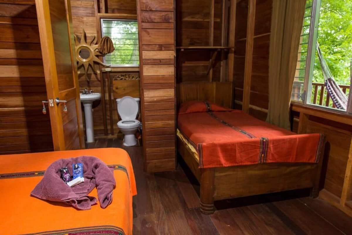 A wooden cabin room with a bed, a window, a toilet, and a sun decoration.