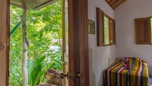 An open doorway leading to a room with a bed, framed pictures on the wall, and a view of greenery outside.