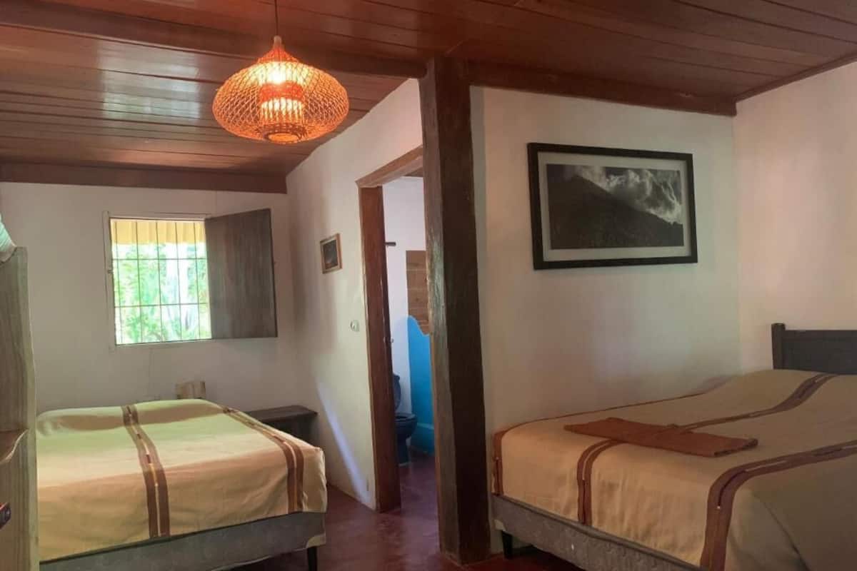 A room with two beds, a hanging light fixture, a framed picture on the wall, and a window with bars.