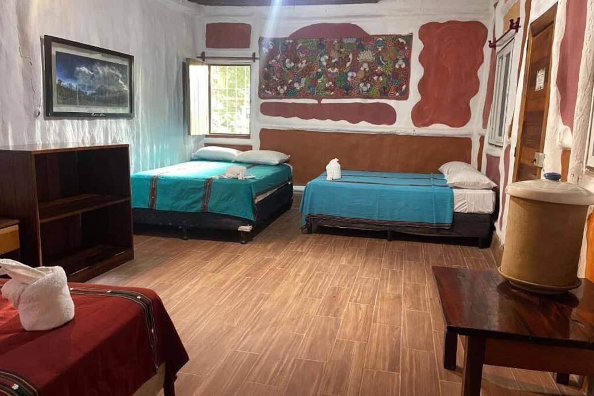 A room with two beds, a wooden floor, a television, and a large tapestry on the wall.