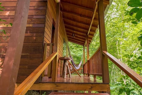 A wooden deck with a hammock and a table, surrounded by lush greenery.